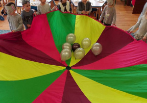 Zabawa z chustą animacyjną – dzieci podrzucają na niej szare balony.